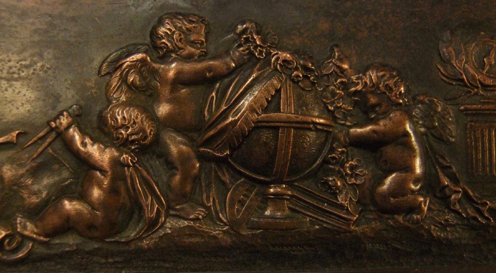 A long horizontal dark bronze relief frieze featuring classical cherubs engaged in allegorical scenes set within a slender rectangular frame. View VII