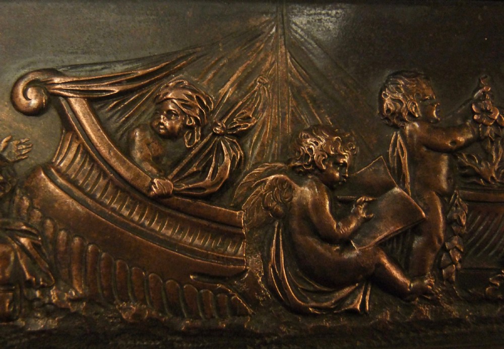 A long horizontal dark bronze relief frieze featuring classical cherubs engaged in allegorical scenes set within a slender rectangular frame. View IX