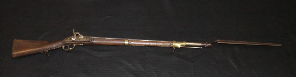 A mid-19th-century French percussion carbine featuring a dark walnut stock, brass fittings, a steel barrel, and an attached socket bayonet against a black background.