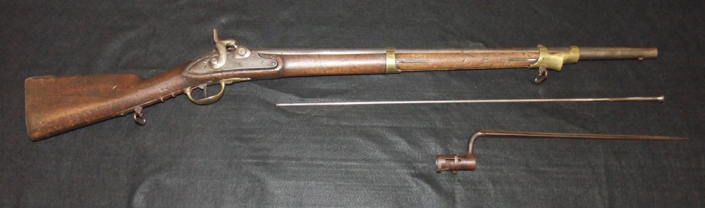 A mid-19th-century French percussion carbine featuring a dark walnut stock, brass fittings, a steel barrel, and an attached socket bayonet against a black background. View II