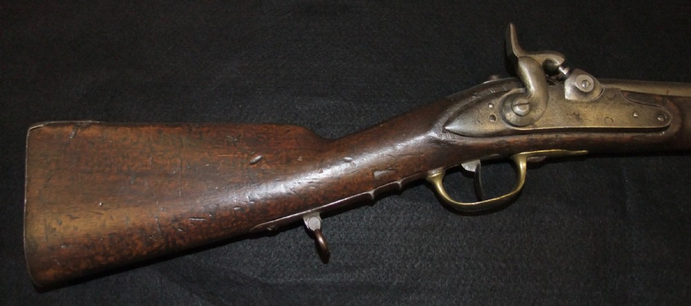 A mid-19th-century French percussion carbine featuring a dark walnut stock, brass fittings, a steel barrel, and an attached socket bayonet against a black background. View XIV
