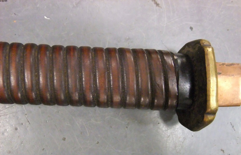 A Japanese WWII officers Shin-Gunto katana featuring a leather-wrapped scabbard, ribbed handle, and brass tsuba. View VII