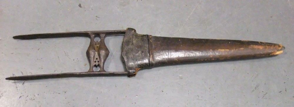 An antique Indian Katar push dagger featuring a dark iron H-shaped handle with double crossbars beside its tapered leather scabbard.