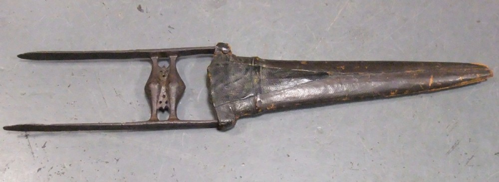 An antique Indian Katar push dagger featuring a dark iron H-shaped handle with double crossbars beside its tapered leather scabbard. View II