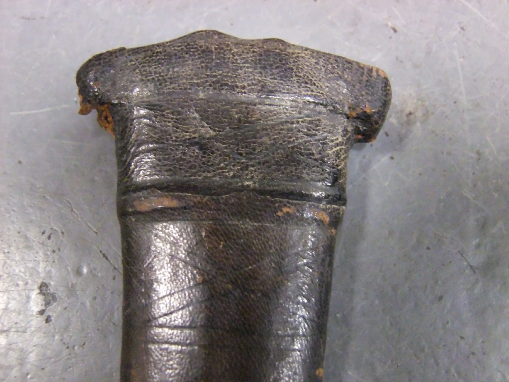 An antique Indian Katar push dagger featuring a dark iron H-shaped handle with double crossbars beside its tapered leather scabbard. View XII