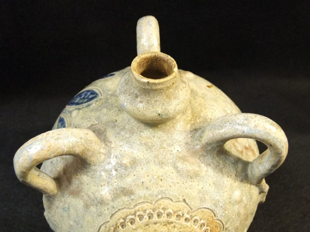 A rounded salt-glazed stoneware flask featuring two top loop handles and a central circular heraldic medallion in neutral grey and beige tones. View V