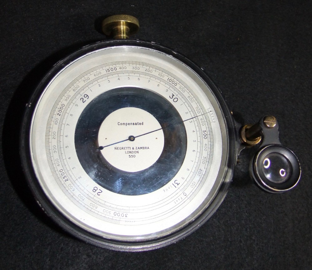 An antique Edwardian black cased aneroid surveying barometer positioned alongside its brown leather carrying case. View IV