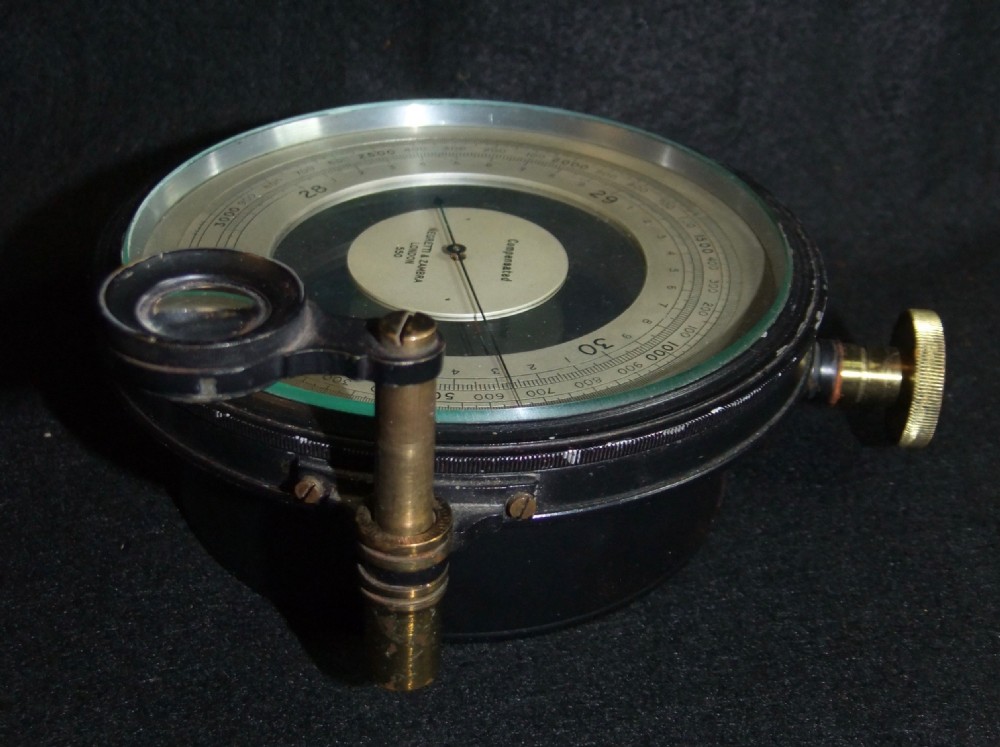 An antique Edwardian black cased aneroid surveying barometer positioned alongside its brown leather carrying case. View VI