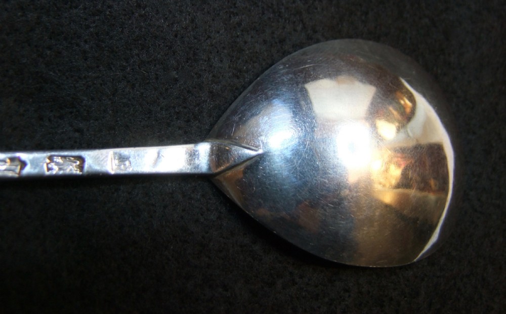 A solid silver spoon featuring a rounded fig-shaped bowl and a straight stem with an obliquely cut slip top end against a dark background. View IX