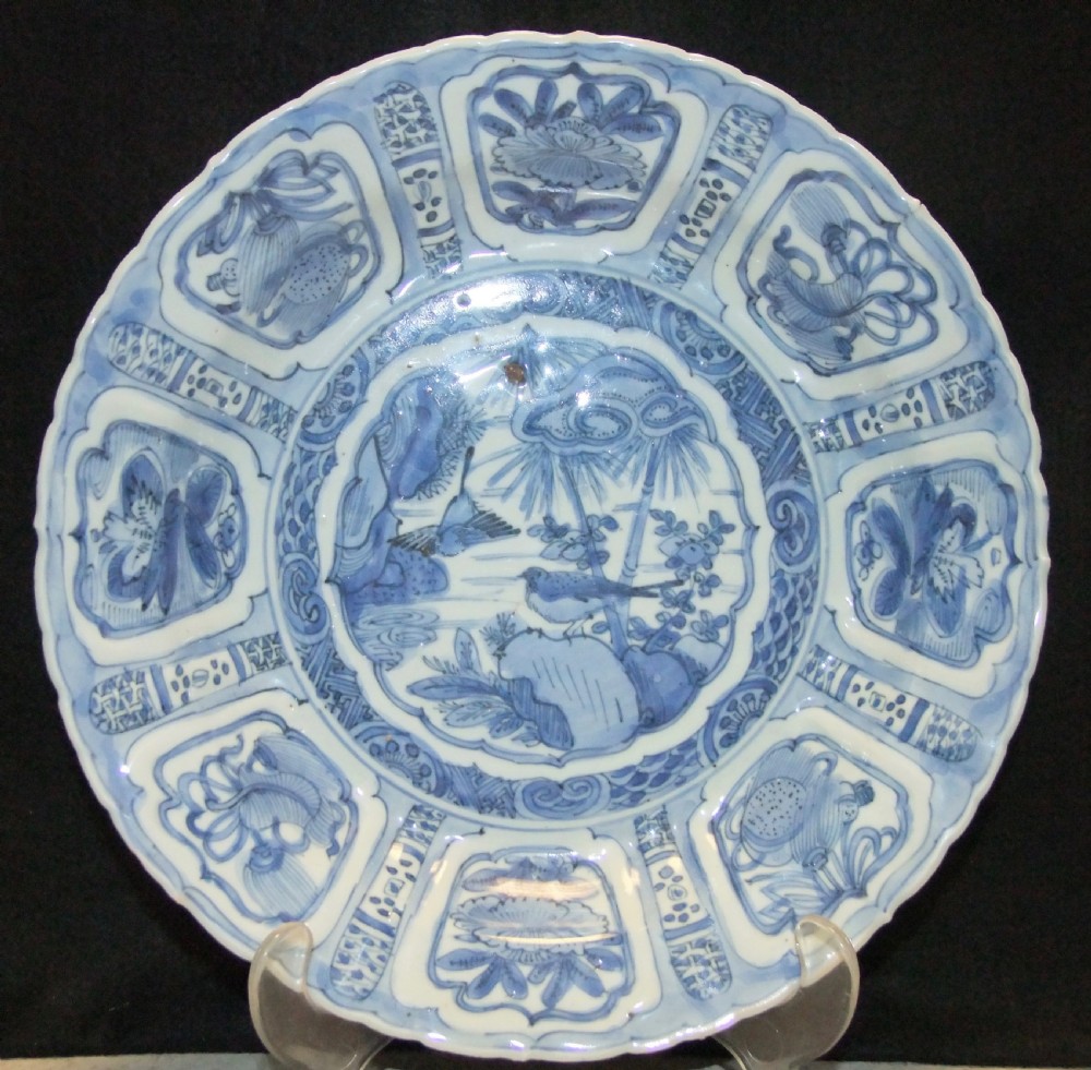 A Chinese Wanli Kraak porcelain deep plate decorated in underglaze blue with central birds and plants surrounded by a panelled rim with a scalloped edge.