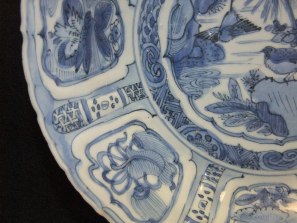 A Chinese Wanli Kraak porcelain deep plate decorated in underglaze blue with central birds and plants surrounded by a panelled rim with a scalloped edge. View V