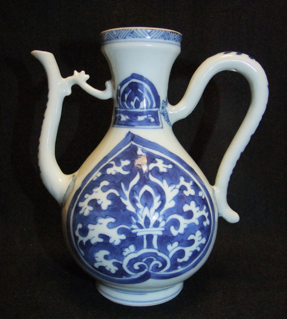 A blue and white Chinese porcelain wine ewer featuring an elongated curved handle, a tall spout with a connecting strut, and painted floral medallion motifs.