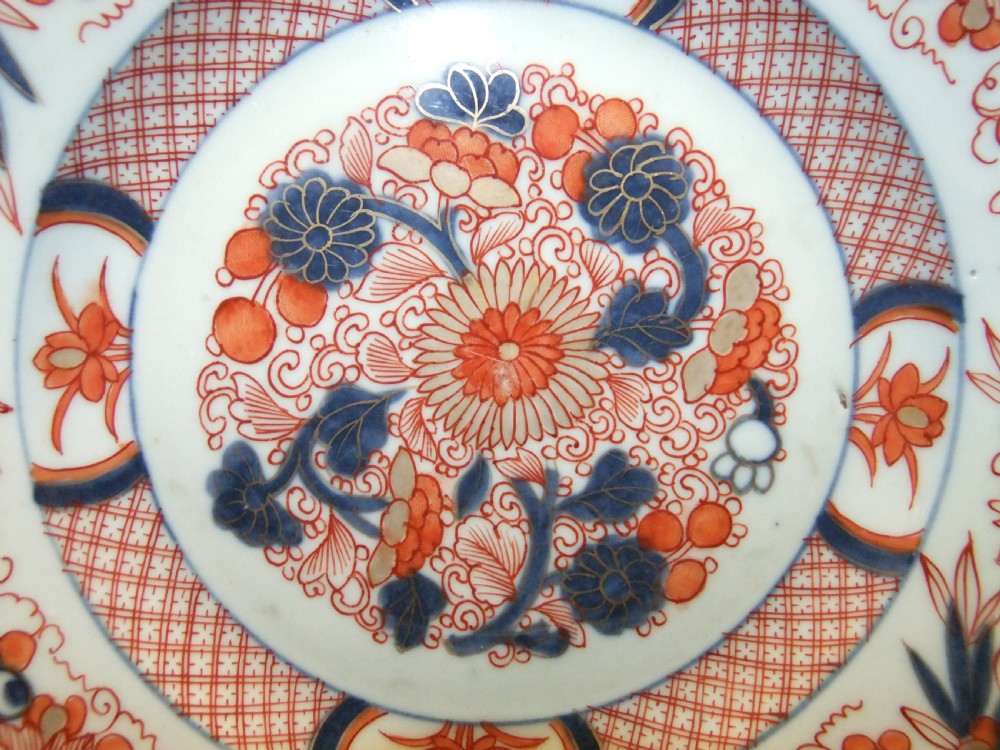 A pair of circular Japanese Edo Period Imari porcelain plates featuring intricate floral motifs in underglaze blue, iron red, and gold gilding on a white ground. View X