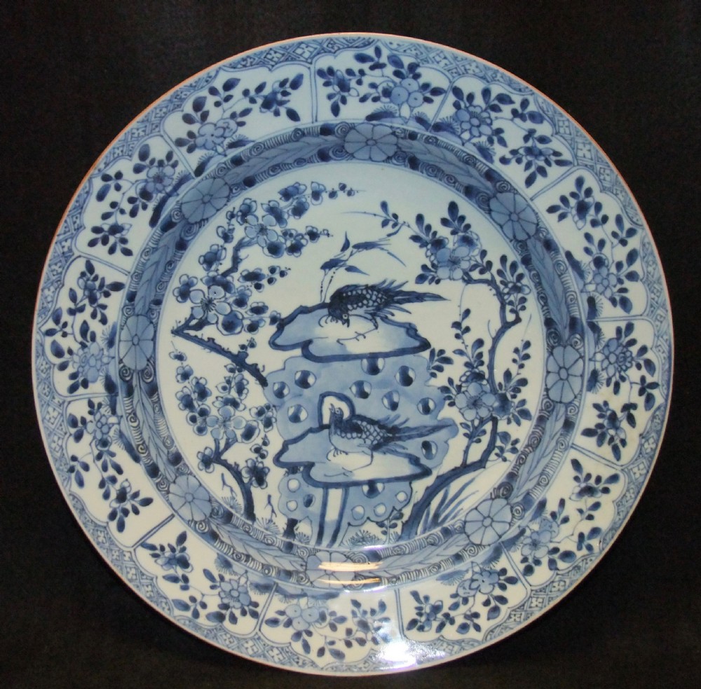 A circular Chinese Kangxi period blue and white porcelain charger featuring hand-painted birds on rockwork surrounded by flowering prunus branches and a decorative panelled border.