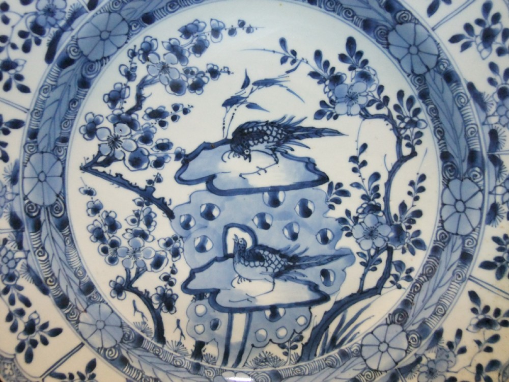 A circular Chinese Kangxi period blue and white porcelain charger featuring hand-painted birds on rockwork surrounded by flowering prunus branches and a decorative panelled border. View II