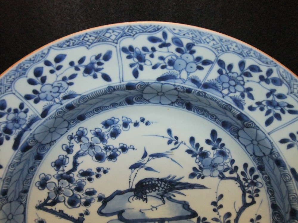 A circular Chinese Kangxi period blue and white porcelain charger featuring hand-painted birds on rockwork surrounded by flowering prunus branches and a decorative panelled border. View III