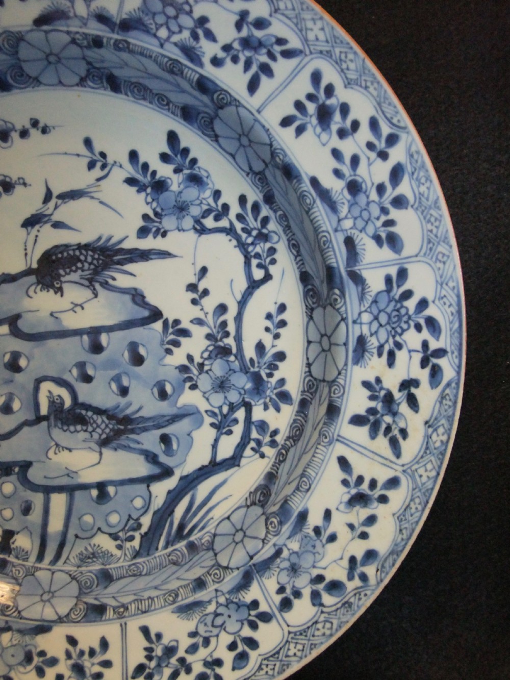 A circular Chinese Kangxi period blue and white porcelain charger featuring hand-painted birds on rockwork surrounded by flowering prunus branches and a decorative panelled border. View IV
