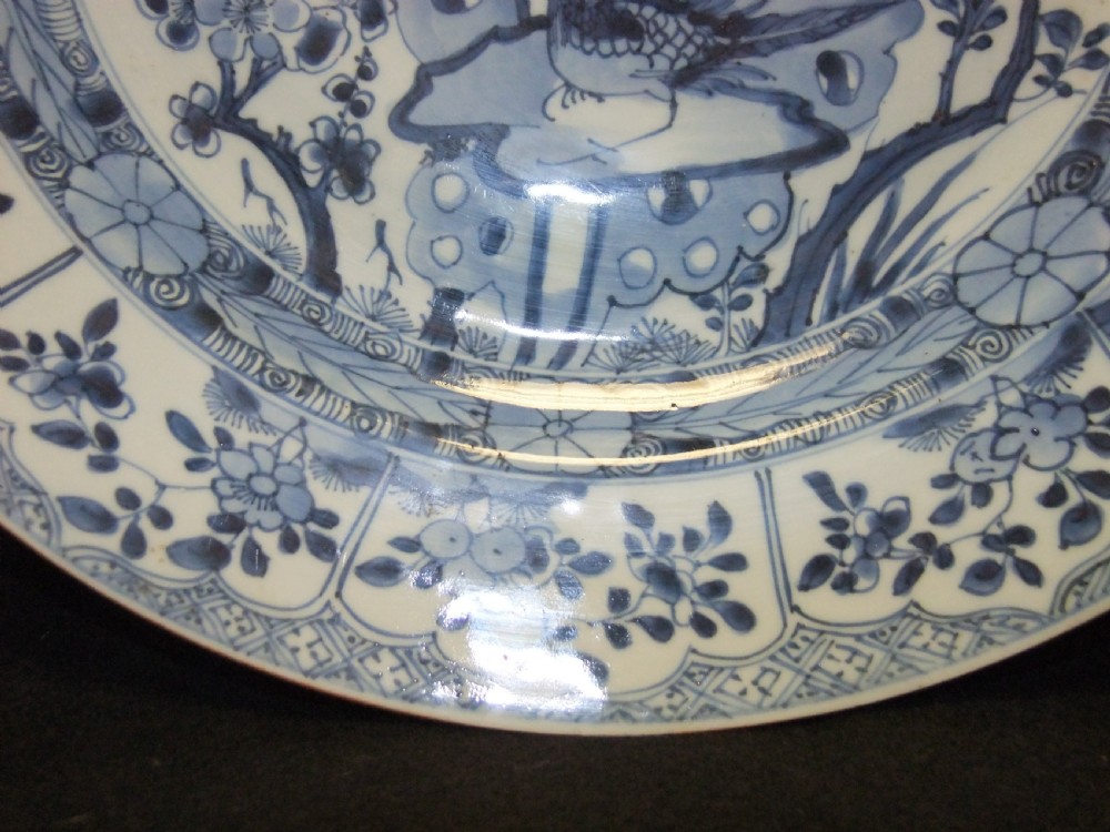 A circular Chinese Kangxi period blue and white porcelain charger featuring hand-painted birds on rockwork surrounded by flowering prunus branches and a decorative panelled border. View V