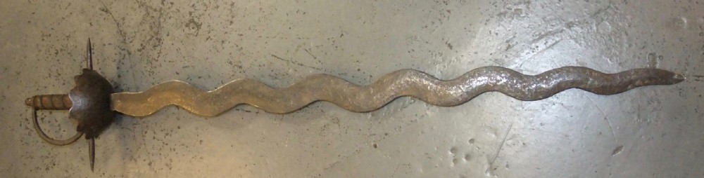 A 17th-century steel cup-hilt sword featuring a long wavy flamberge blade and a rounded metal hand guard. View XIX