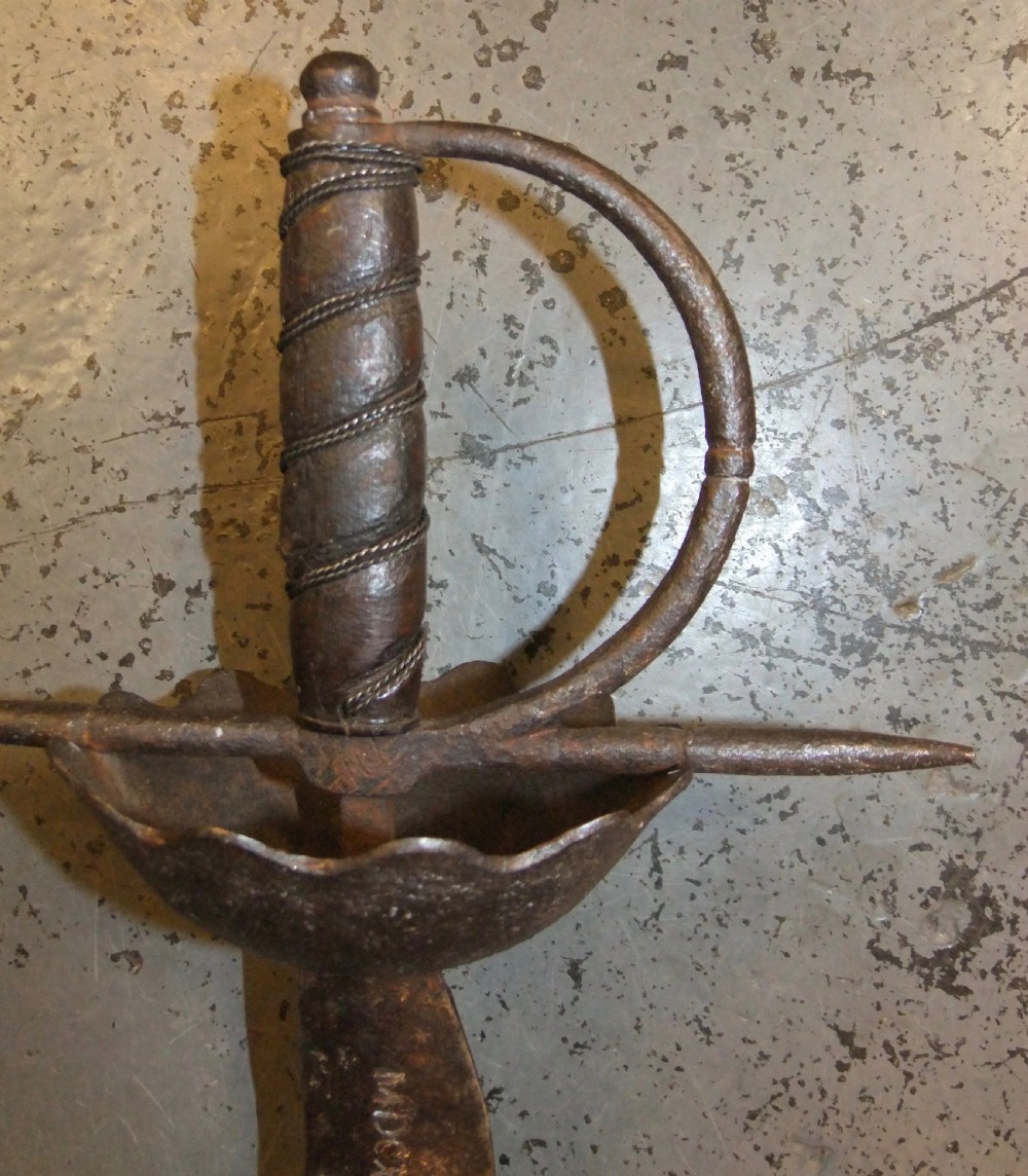 A 17th-century steel cup-hilt sword featuring a long wavy flamberge blade and a rounded metal hand guard. View XXV
