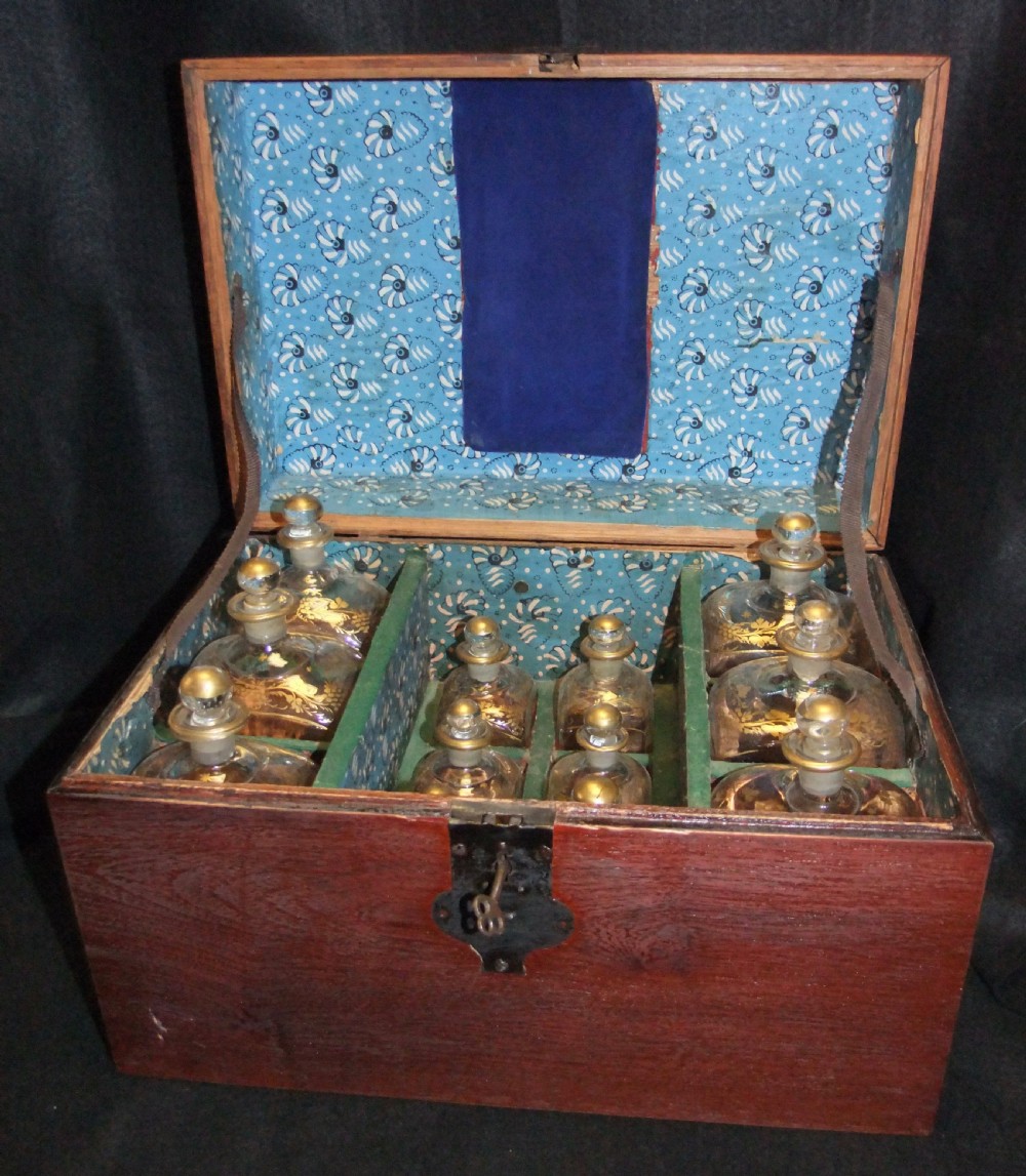 An open wooden campaign box with a blue patterned fabric lining containing ten gilded glass decanters and matching glass stoppers.