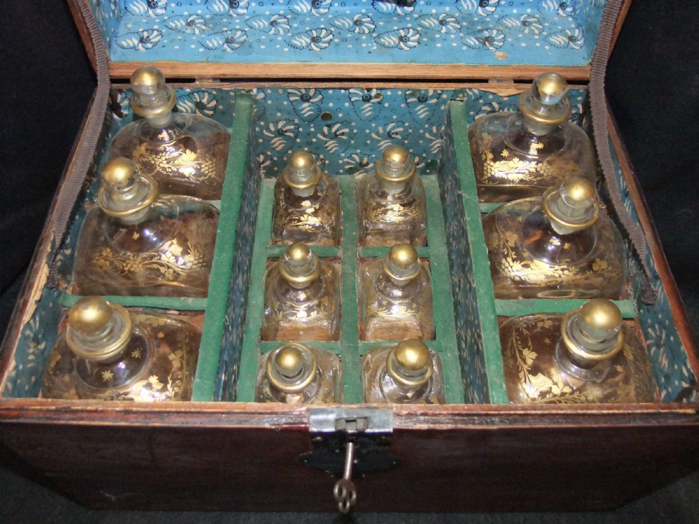 An open wooden campaign box with a blue patterned fabric lining containing ten gilded glass decanters and matching glass stoppers. View II