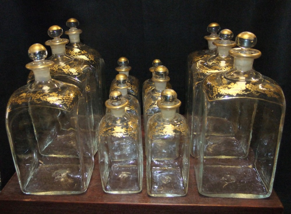 An open wooden campaign box with a blue patterned fabric lining containing ten gilded glass decanters and matching glass stoppers. View III