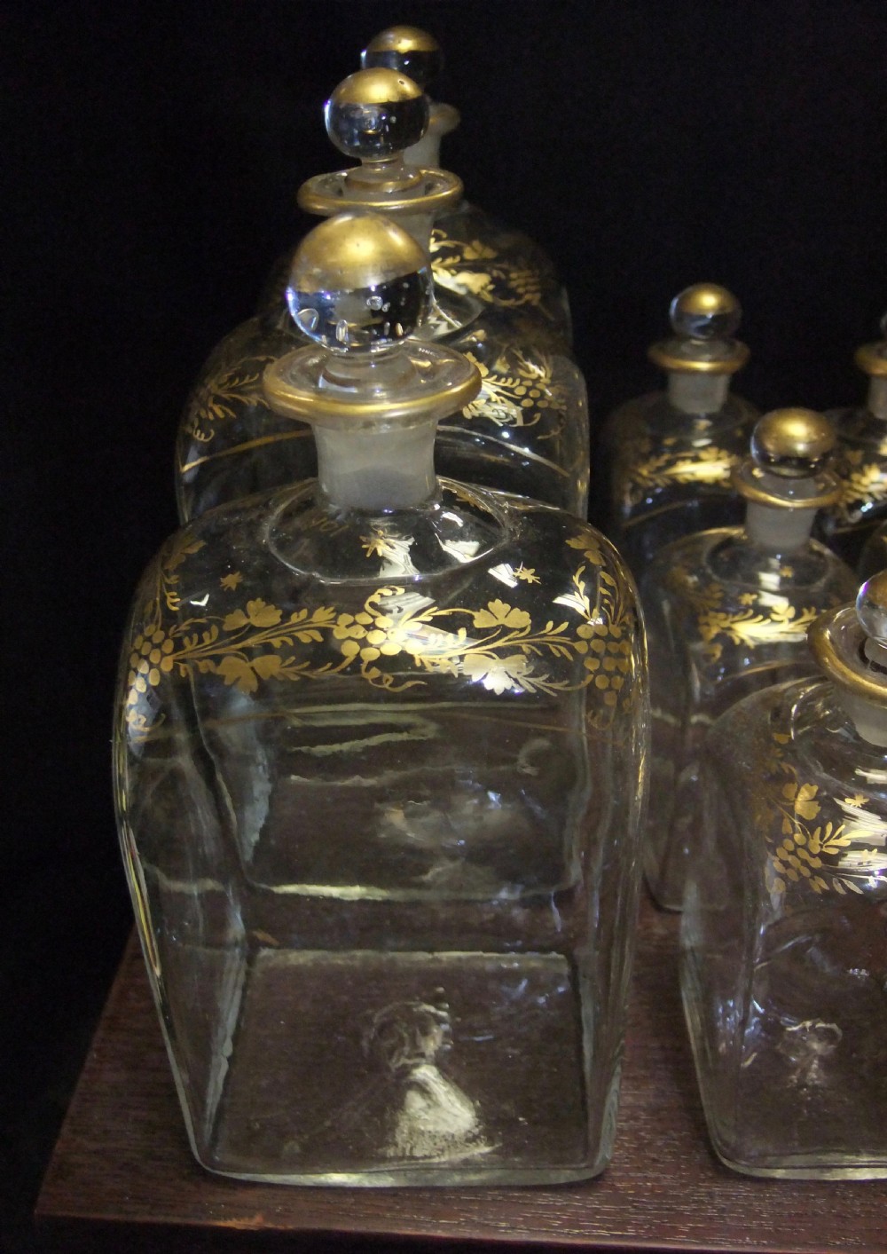 An open wooden campaign box with a blue patterned fabric lining containing ten gilded glass decanters and matching glass stoppers. View V