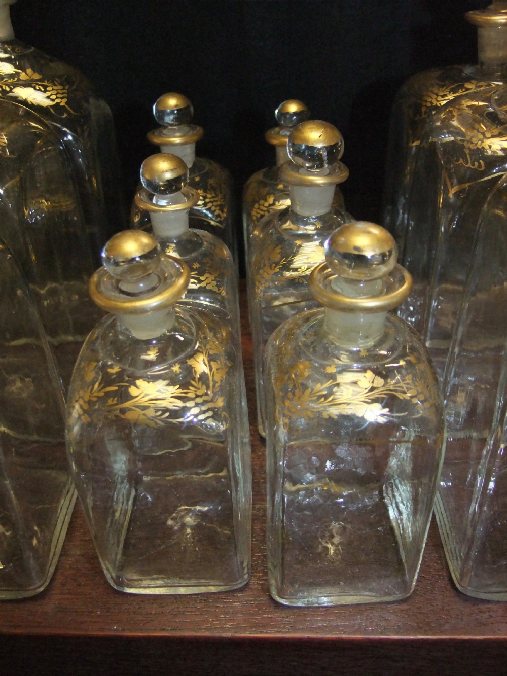 An open wooden campaign box with a blue patterned fabric lining containing ten gilded glass decanters and matching glass stoppers. View VI