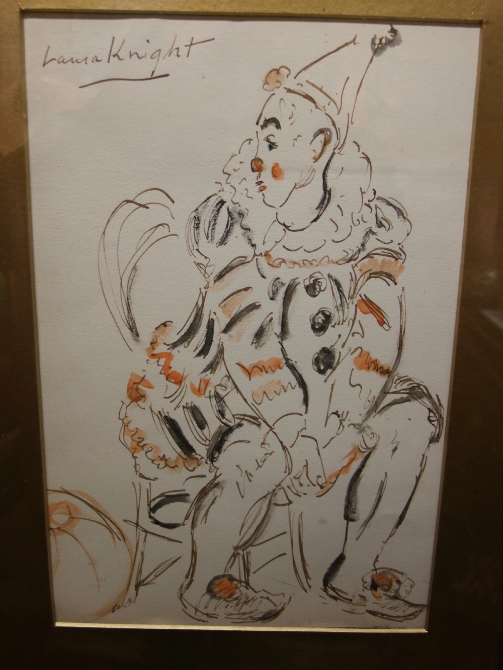 An ink and watercolour sketch depicting a seated clown in costume, signed Laura Knight in the upper left corner.