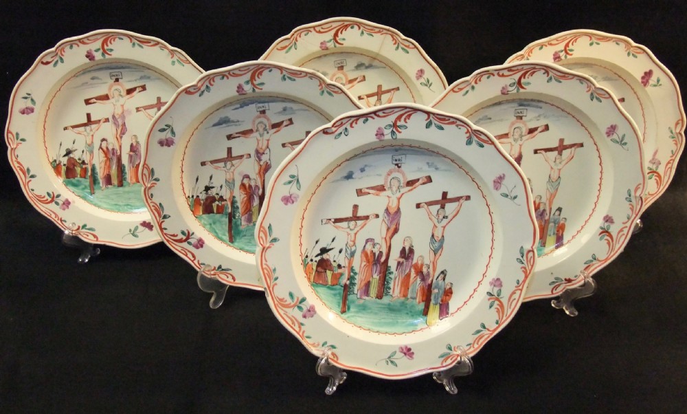 A set of six cream-coloured earthenware plates decorated with hand-painted scenes of the Crucifixion and floral scroll borders along scalloped rims.