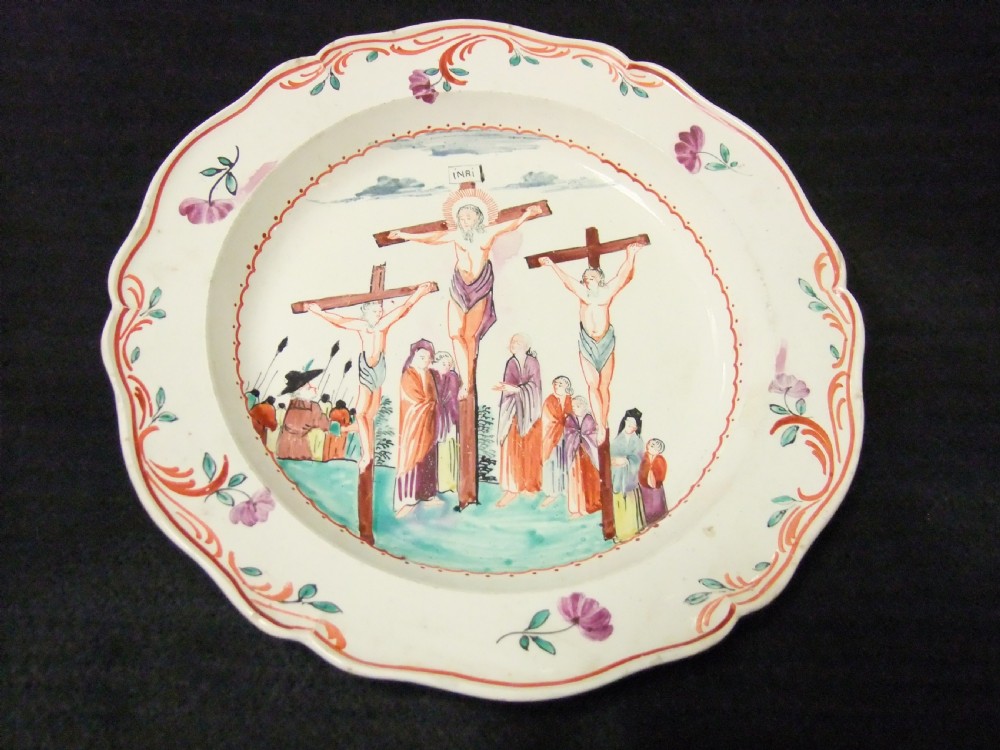 A set of six cream-coloured earthenware plates decorated with hand-painted scenes of the Crucifixion and floral scroll borders along scalloped rims. View II