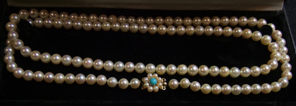An opera length strand of cream freshwater pearls featuring a flower-shaped gold clasp set with a cabochon turquoise centre.