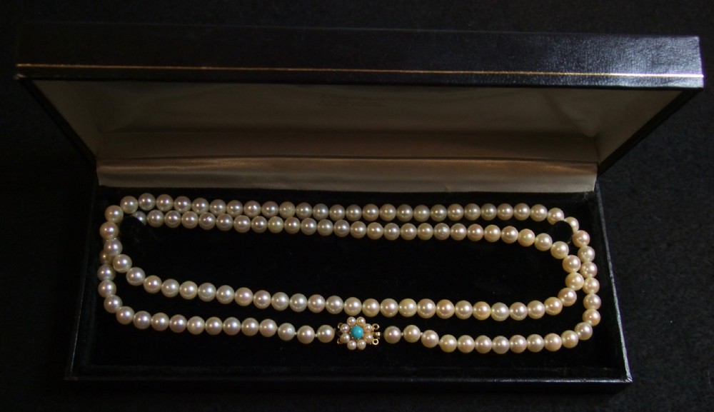 An opera length strand of cream freshwater pearls featuring a flower-shaped gold clasp set with a cabochon turquoise centre. View II