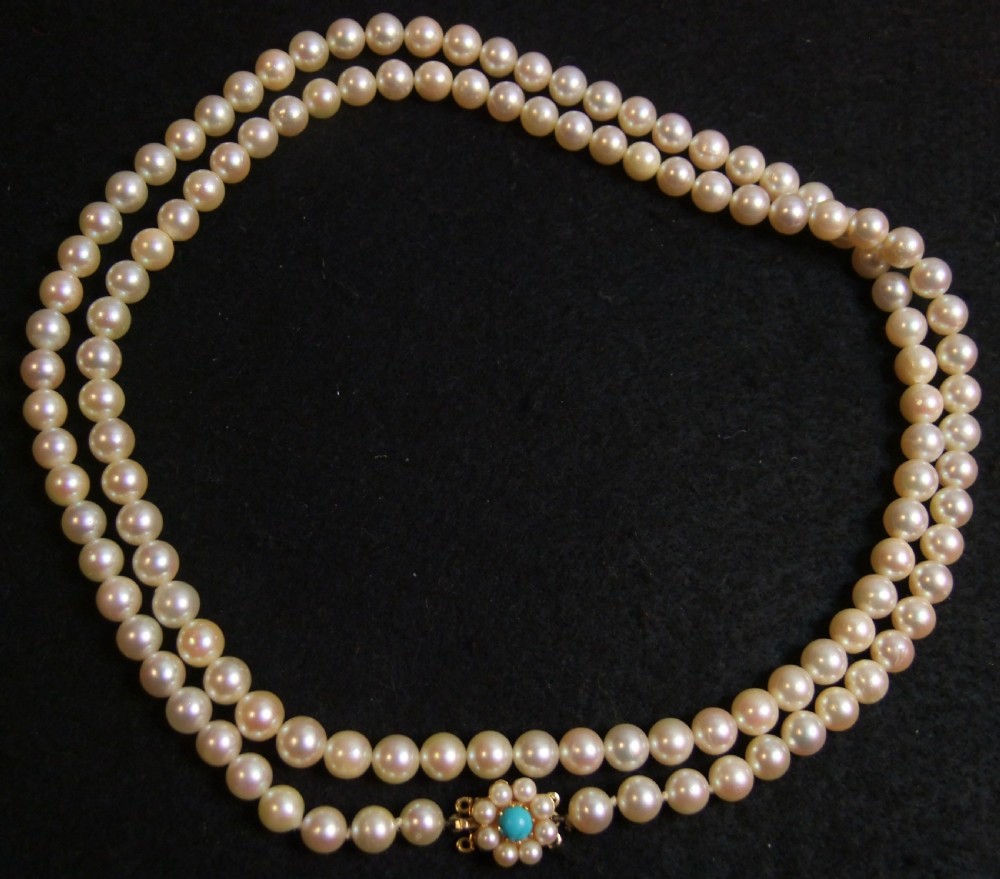 An opera length strand of cream freshwater pearls featuring a flower-shaped gold clasp set with a cabochon turquoise centre. View VI
