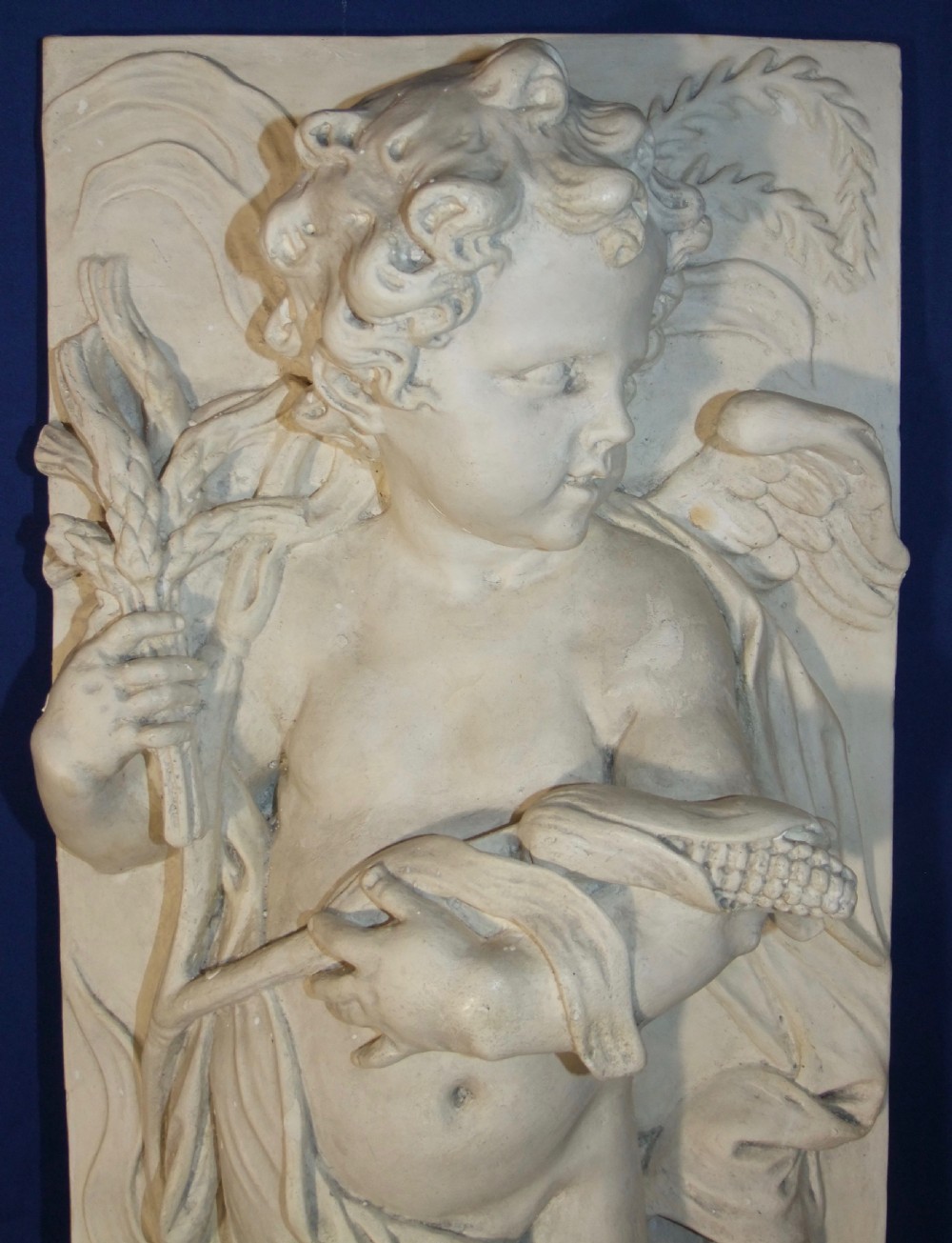 A pair of vertical off-white plaster relief friezes depicting winged cherubs holding wheat sheaves and a chalice with grapes. View III