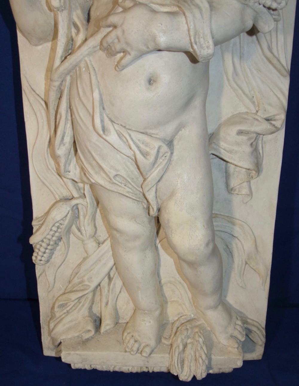 A pair of vertical off-white plaster relief friezes depicting winged cherubs holding wheat sheaves and a chalice with grapes. View IV