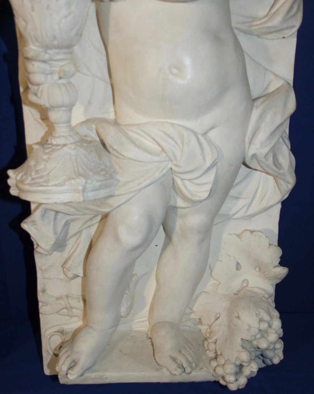 A pair of vertical off-white plaster relief friezes depicting winged cherubs holding wheat sheaves and a chalice with grapes. View VII