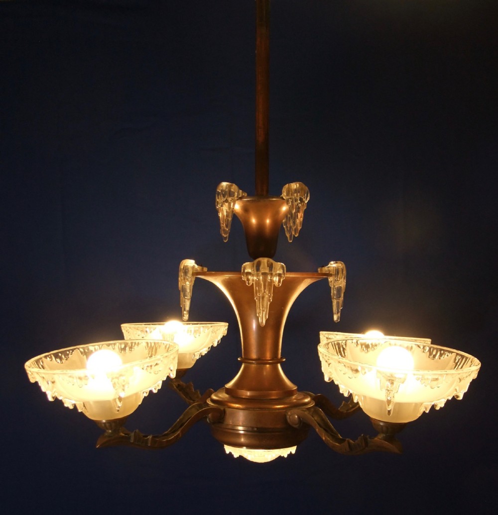 An Art Deco copper chandelier featuring a flared central stem, decorative glass icicle motifs, and four frosted glass shades fitted with light bulbs.