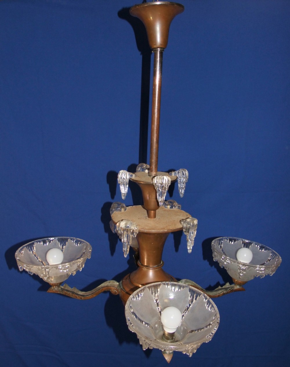An Art Deco copper chandelier featuring a flared central stem, decorative glass icicle motifs, and four frosted glass shades fitted with light bulbs. View V