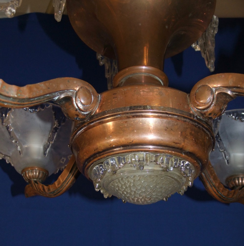 An Art Deco copper chandelier featuring a flared central stem, decorative glass icicle motifs, and four frosted glass shades fitted with light bulbs. View IX
