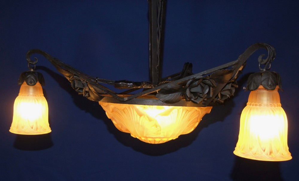 An Art Nouveau wrought metal chandelier featuring a central frosted amber glass bowl surrounded by sculpted rose leaves and two suspended glass shades.
