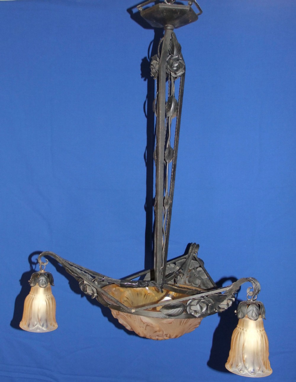 An Art Nouveau wrought metal chandelier featuring a central frosted amber glass bowl surrounded by sculpted rose leaves and two suspended glass shades. View VI