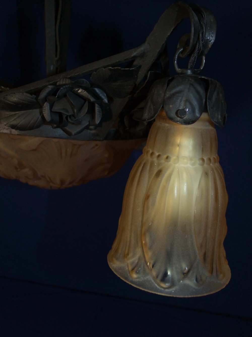 An Art Nouveau wrought metal chandelier featuring a central frosted amber glass bowl surrounded by sculpted rose leaves and two suspended glass shades. View VIII
