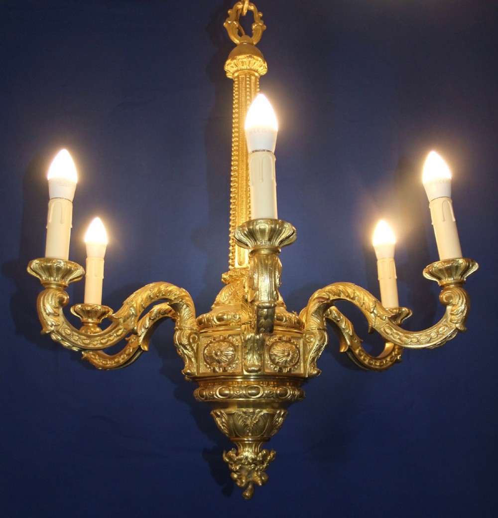 A six-arm gilt bronze chandelier in the Baroque style featuring scrolling arms, acanthus leaf detailing, and candle-style bulb sleeves.