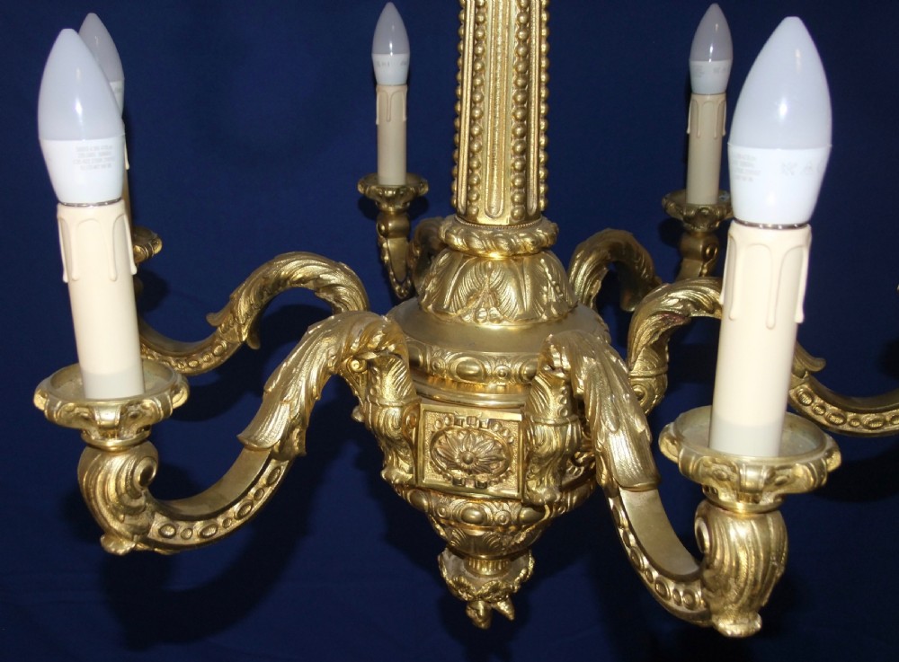 A six-arm gilt bronze chandelier in the Baroque style featuring scrolling arms, acanthus leaf detailing, and candle-style bulb sleeves. View VII