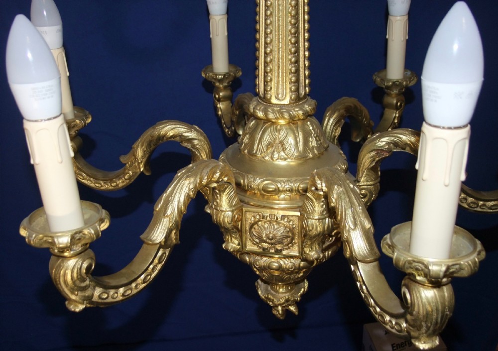 A six-arm gilt bronze chandelier in the Baroque style featuring scrolling arms, acanthus leaf detailing, and candle-style bulb sleeves. View IX