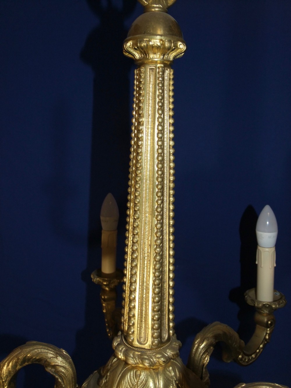 A six-arm gilt bronze chandelier in the Baroque style featuring scrolling arms, acanthus leaf detailing, and candle-style bulb sleeves. View X