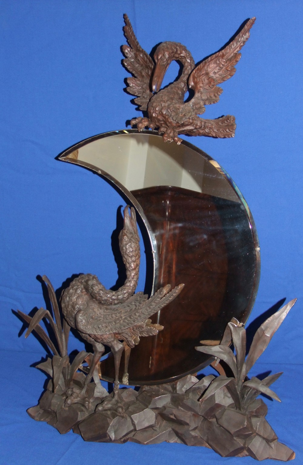 A late 19th-century carved wood mirror featuring a crescent moon-shaped glass surrounded by detailed carvings of wading birds and reeds.