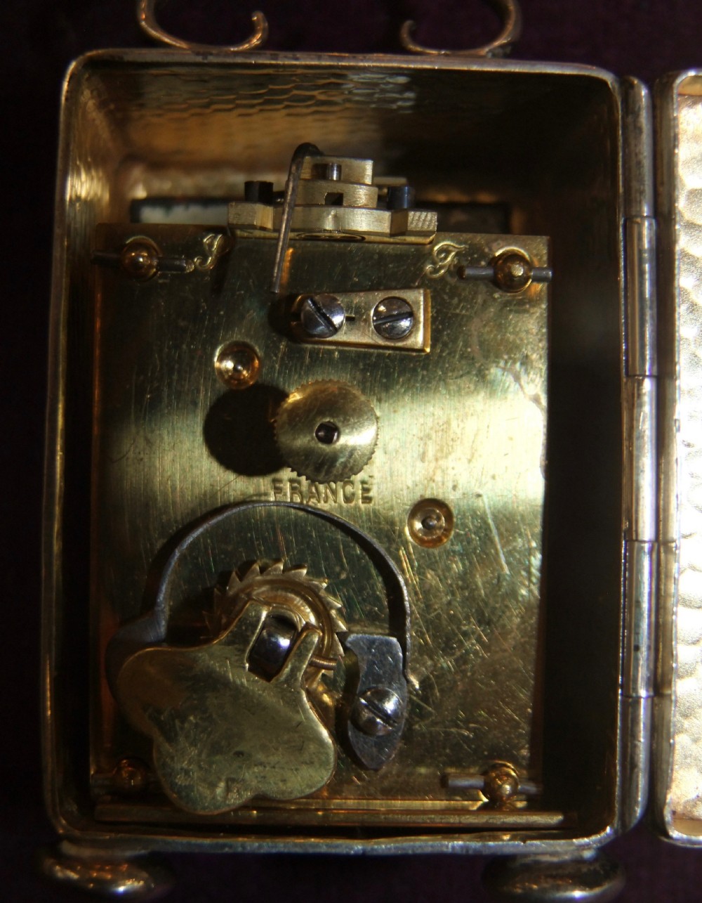 An Edwardian sterling silver carriage clock featuring a hand-planished finish, a curved top handle, small ball feet, and a white enamel dial with black Roman numerals. View VII